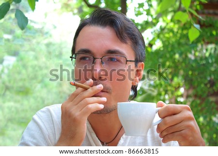Young handsome man smoking cigar and drinking coffee