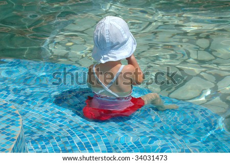 Small girl sits on step of the water pool