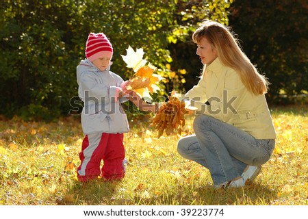 Young woman and child collect autumn sheets in park