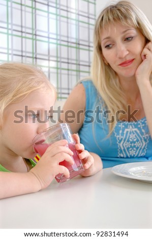 The little girl drinks a pink drink from a glass