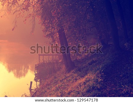 Vintage photo of landscape with autumn forest and foggy lake in sunrise