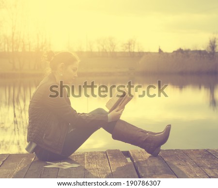 Woman reading a book in sunset at the lake