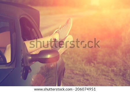 Vintage photo of woman\'s legs in retro shoes out of car windows in summer sunset