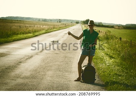 Vintage photo of traveler woman hitchhiking along lonely road in summer sunset