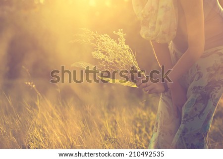 Vintage photo of woman with bunch of wild flowers in sunset