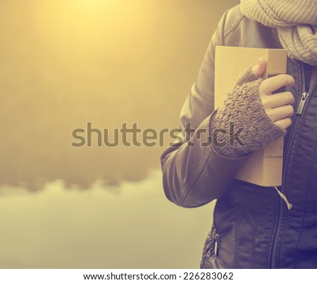 Woman standing with a book at the lake in sunset