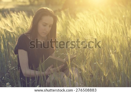 Woman with a book on wheat field in sunset