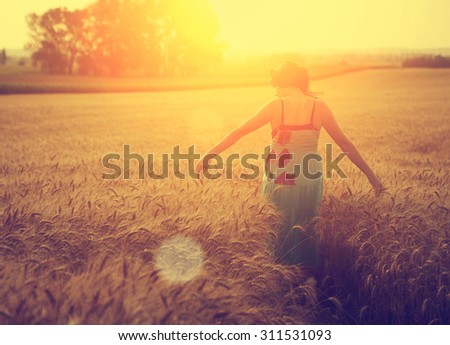 Woman walking on wheat field in sunset