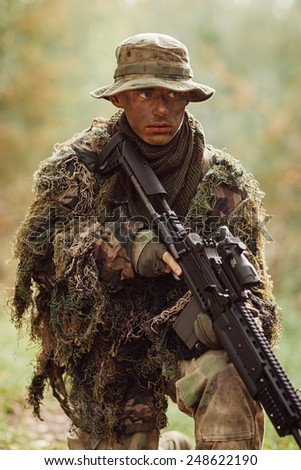 soldier stands with arms in wood and looks forward