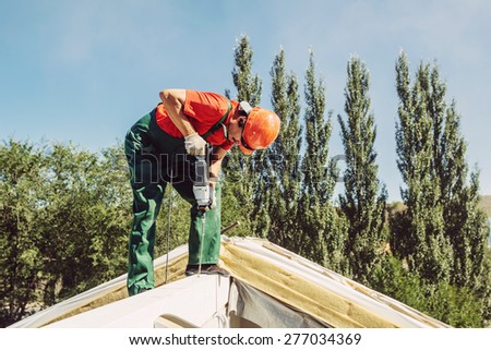 adult roofer using a drill is fastening a cap to a house roof