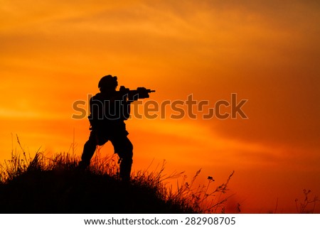 Silhouette of military soldier or officer with weapons at sunset. shot, holding gun, colorful sky, background