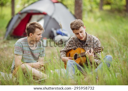Two young friend sitting in the tent, play the guitar and sing songs
