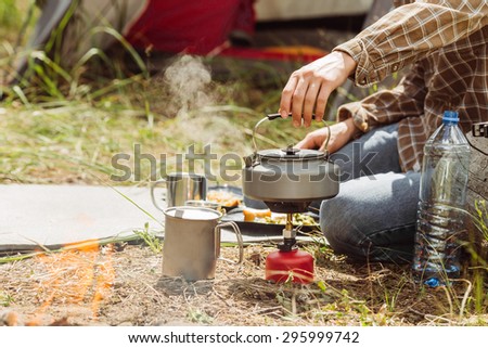 A person boiling water in a pot over a propane stove to make tea