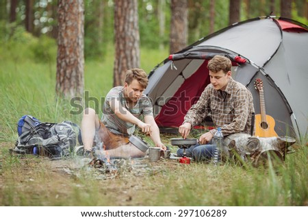 Two fellow campers making tea and preparing food by a tent in the forest