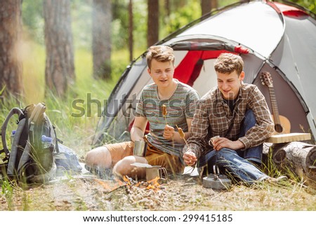 Two young men are heated in a fire and cook out on a summer forest