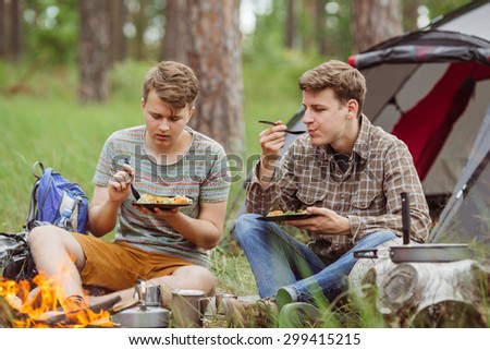 Two young men are heated in a fire and cook out on a summer camp