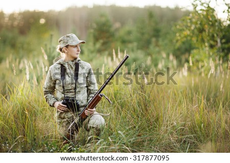 woman hunter with shotgun looking through binoculars in forest