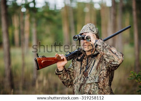 man hunter with shotgun looking through binoculars in forest