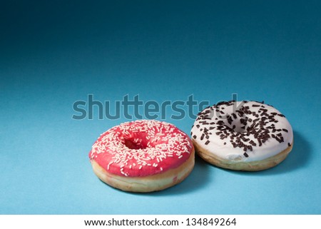 two donuts with red and white icing isolated on blue background with copyspace
