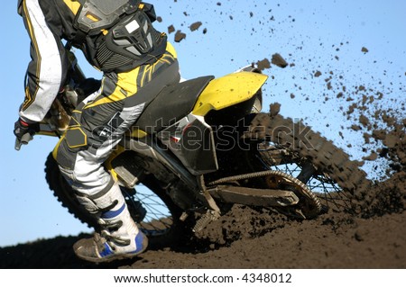 A rear view of a motocross rider races through the dirt and mud during a race.