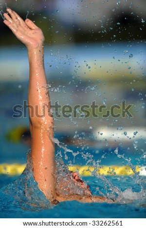 A male backstroke swimmer in action during a competition with water drops coming off his arm.