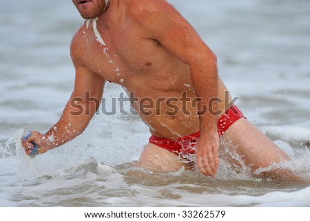 A male surf lifesaver (triathlon) runs out of the ocean during a competition.
