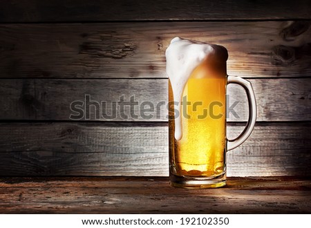 Mug of light beer with foam on wooden table