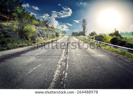 Asphalt road in a mountainous area under a dramatic sky with a huge sun side