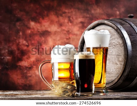 Mugs and glasses with light and dark beer on background wooden barrel