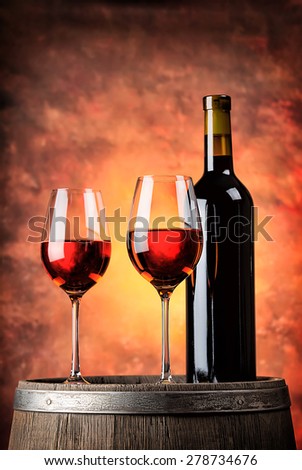 Bottle and two glasses of red wine on wooden barrel with red background