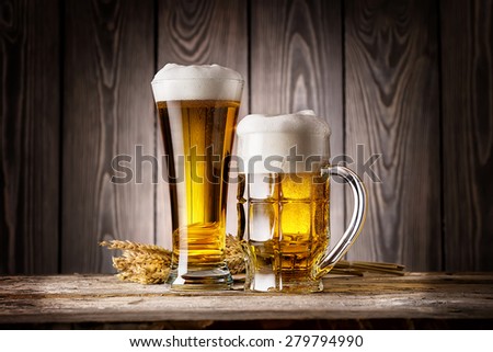 Tall glass and mug of light beer with ears barley on wooden background