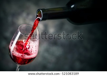 Red wine is being poured into glass shot against dark background