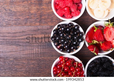 row of wild berries in bowls on wooden background