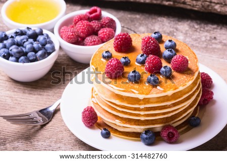 Pancakes with blueberries , raspberry & honey on wood background .