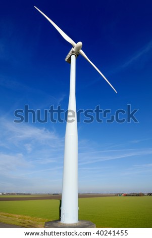 Wind turbine seen from a low point of view, which stand on a flat meadow against a blue sky. On the horizon more windmills can be seen.