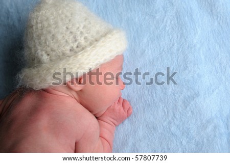 Newborn baby with cap is sleeping on blue blanket.