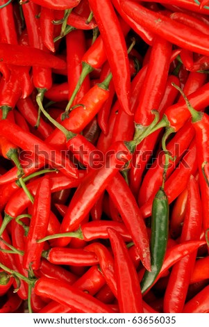 A pile of spicy red hot chili peppers and one green pepper in corner