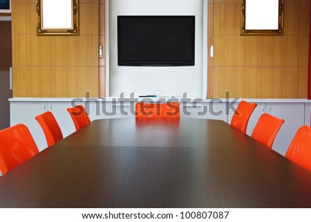 Meeting room with brown table , orange armchairs , television and wood wall