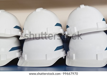 Stack of white plastic safety helmets with blue strip