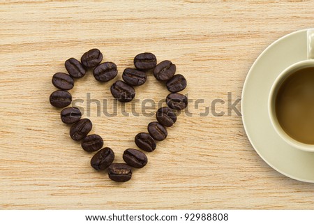 Coffee beans in the form of heart on wooden texture and a cup of coffee