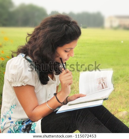Portrait of an Asian / Indian college student thinking while reading a book at campus.