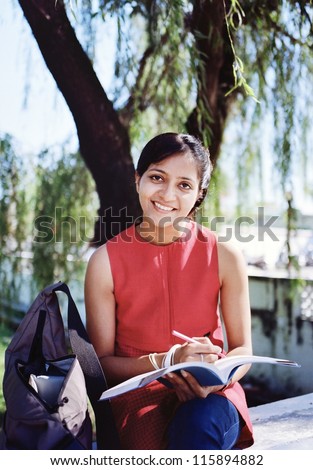 Beautiful Indian / Asian college student writing notes under the tree.