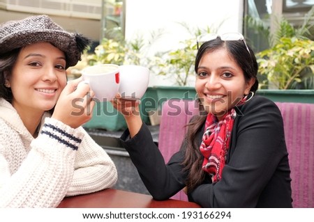 Girls doing cheers with their coffee mugs in a restaurant.