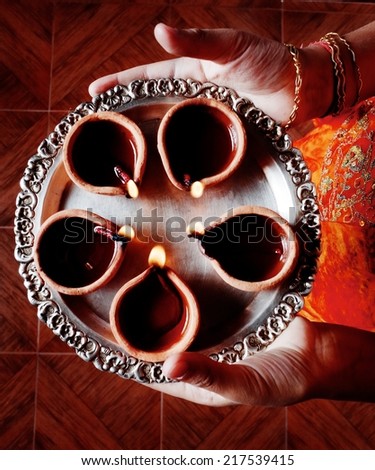 Human hands holding plate of oil lamps on Deepawali in India.