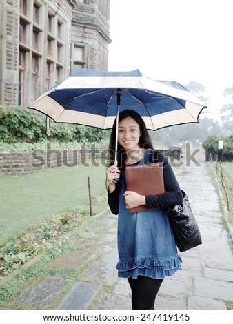 Cheerful Asian student walking through the rain.
