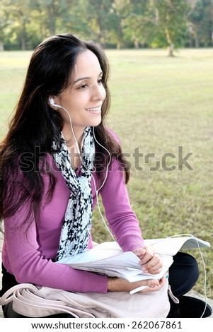 Pretty woman hearing music while studying outdoor.