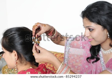 A beautifully dressed Indian lady is pinning a girl\'s hair with an ornamented hairpin.