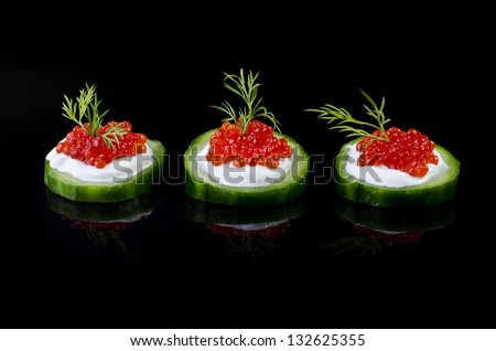 Delicatessen appetizer - red caviar on a green cucumber, isolated on a black background