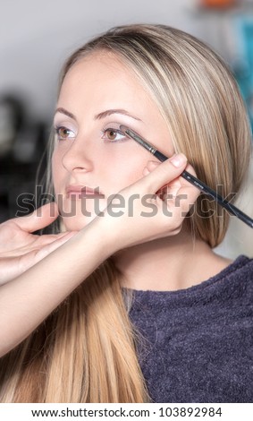 Portrait of beautiful young woman with esthetician making makeup eye shadow