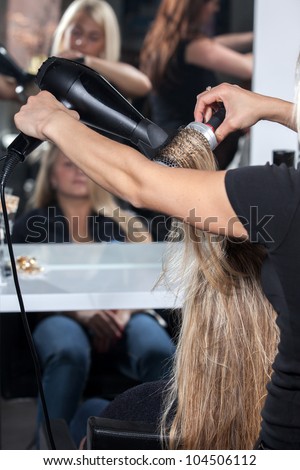 hair stylist with blower work on woman hair in salon